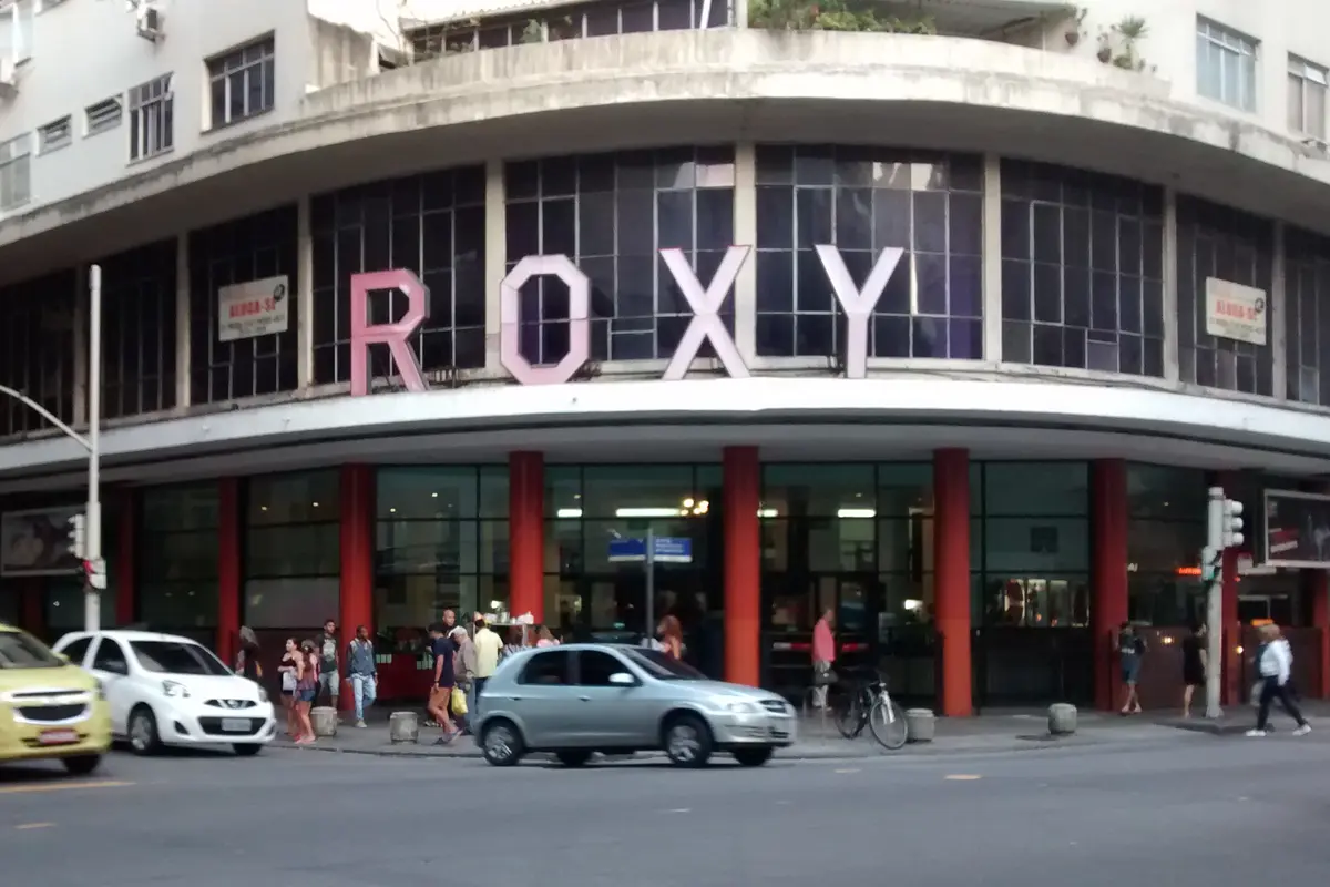 The curved Art Deco corner of the Roxy building in Copacabana, with large pink ROXY letters above red columns at street level