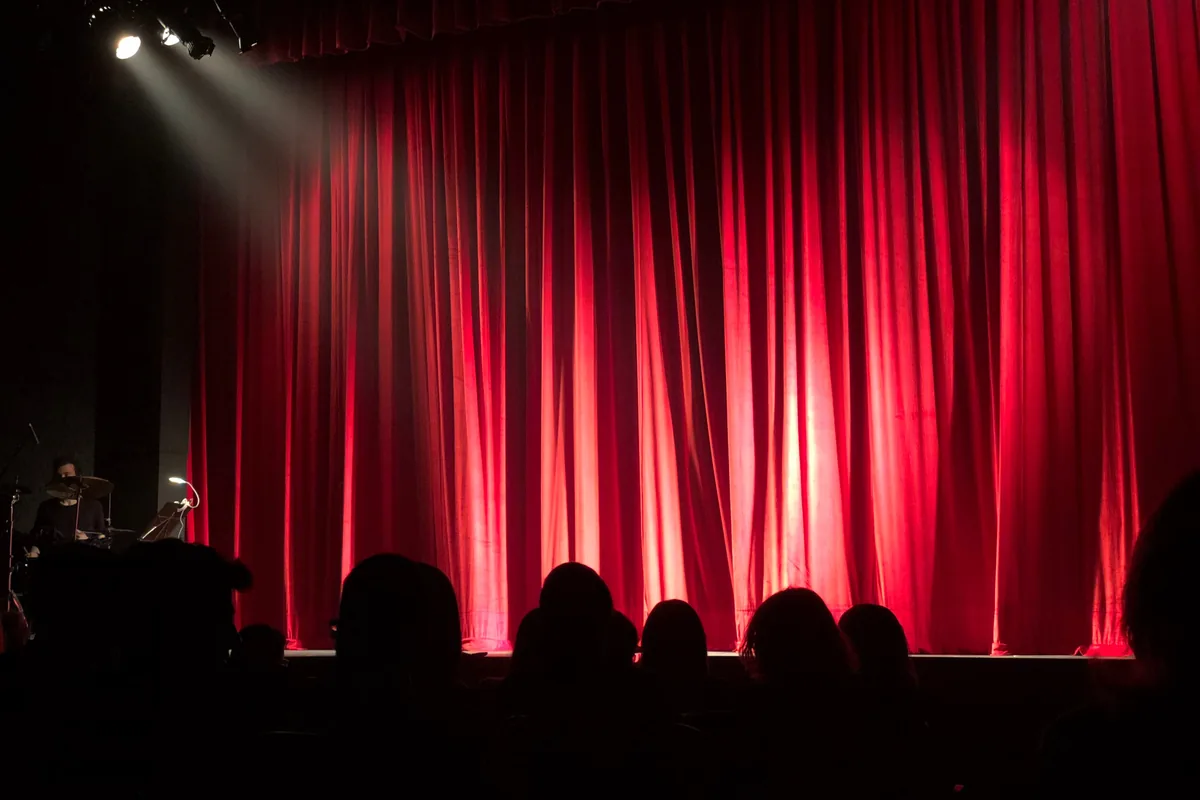 A stage show under coloured lights with an audience in the foreground